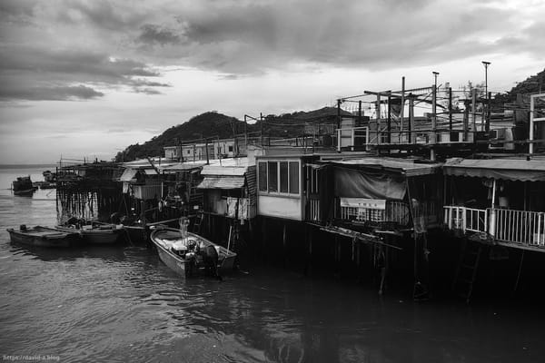 Des maisons sur pilotis et des barques amarrées dans un village de pêcheurs de Hong Kong, sous un ciel couvert.